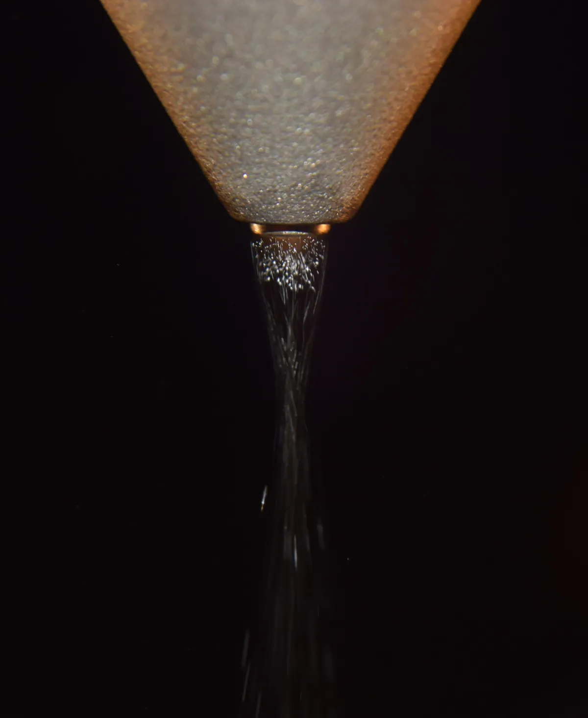 Close-up of a MicroSpray ultrasonic nozzle tip atomizing liquid into a fine spray stream, photographed against a black background